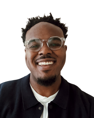 A young Black man with short afro hair, clear glasses and a smile, wearing a black jacket and a white t shirt